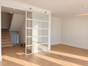 Puerta corredera acristalada con perfilería blanca junto a la escalera, reforma en Alcobendas