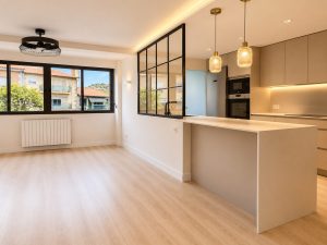 Salón con cerramiento de acero y vidrio hacia la cocina – reforma integral de vivienda en Torrelodones