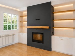 Chimenea negra con estanterías de roble iluminadas en el salón · reforma integral en Torrelodones