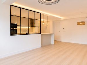 Salón con cerramiento de acero y vidrio hacia la cocina – reforma integral de vivienda en Torrelodones