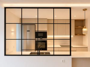 Salón con cerramiento de acero y vidrio hacia la cocina – reforma integral de vivienda en Torrelodones