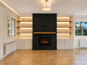 Chimenea negra con estanterías de roble iluminadas en el salón · reforma integral en Torrelodones