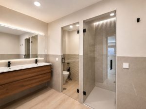 Baño principal con doble lavabo y mueble de madera – reforma integral de vivienda en Torrelodones