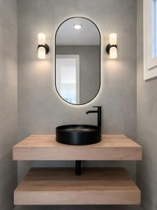 Aseo con lavabo negro sobre encimera de madera y espejo ovalado · reforma integral en Torrelodones