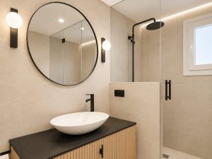 Baño con grifería negra, espejo redondo y mueble de madera · reforma integral en Torrelodones