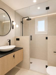 Baño con grifería negra, espejo redondo y mueble de madera · reforma integral en Torrelodones